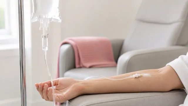 An intravenous line running into a client's forearm beside a treatment chair and a hanging infusion bag