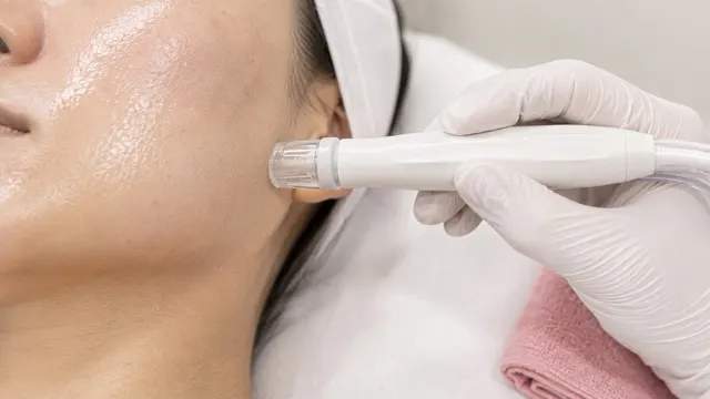 A gloved practitioner drawing a treatment handpiece along a client's cheek